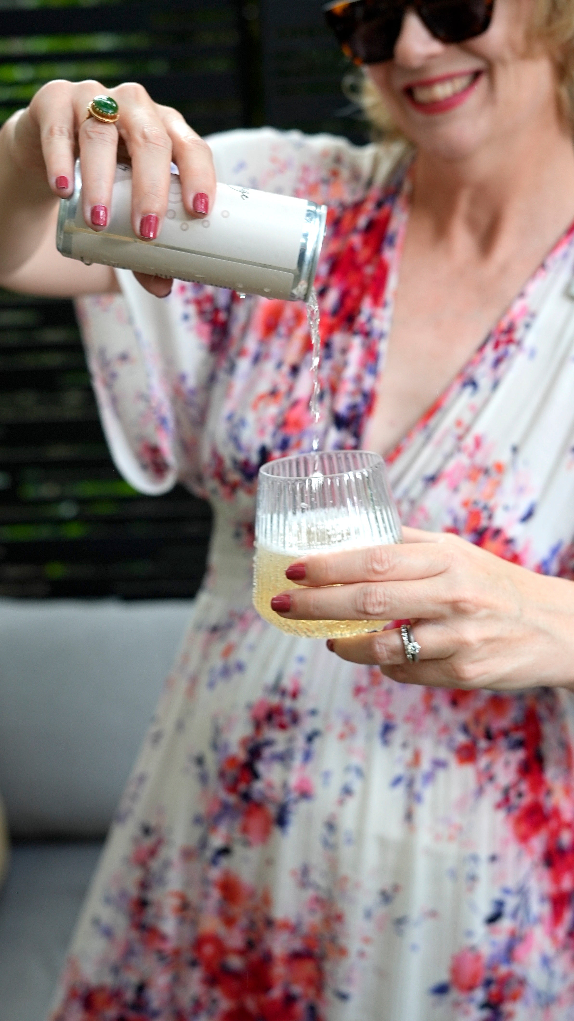 Woman in floral dress pouring canned sparkling drink into ribbed glass outdoors