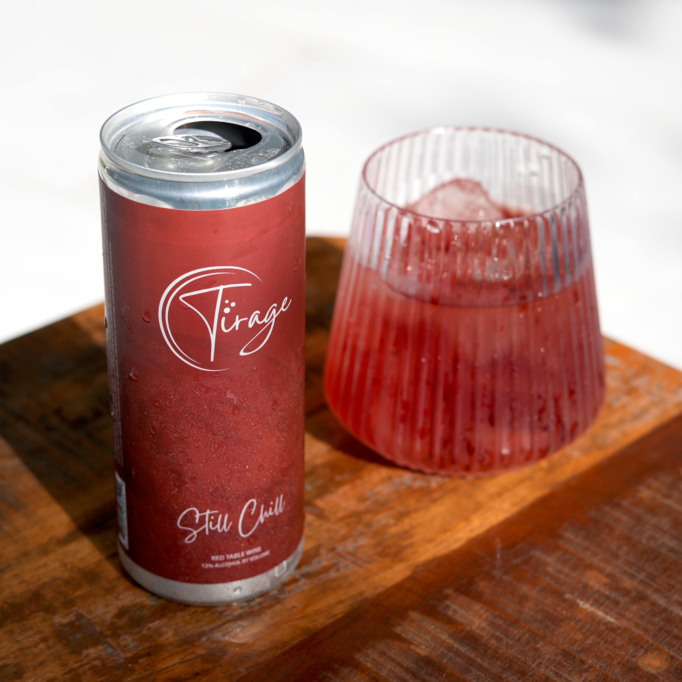 Can of Tirage Still Chill red table wine next to glass with ice on wooden surface